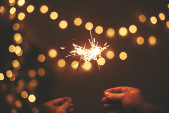 hands holding sparklers with string lights in background