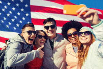 smiling friends taking a selfie in front of the American flag
