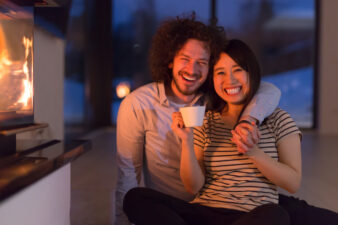 happy multiethnic couple sitting in front of fireplace