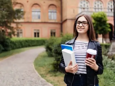American university student smiling with coffee and book bag on campus