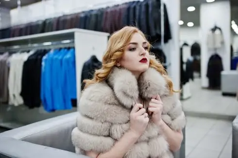 Elegance blonde girl in fur coat at the store of fur coats and leather jackets.